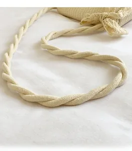 Detail of cream woven shoulder bag featuring thick braided strap and lace bow accent