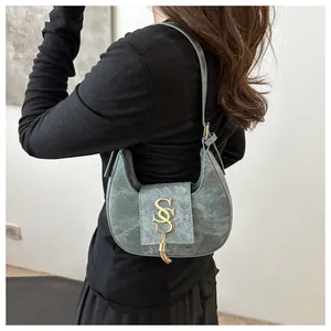 Détail du sac croissant bleu-gris avec logo S doré et glands métalliques porté par un mannequin