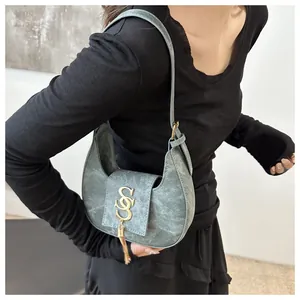Détail du sac croissant bleu avec boucle dorée en S et décorations de glands en métal