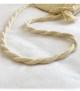Detail of twisted woven shoulder strap and lace bow on a beige straw crossbody bag
