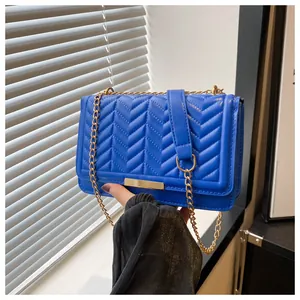 Detail of blue quilted shoulder bag with V-shaped stitching and gold chain strap
