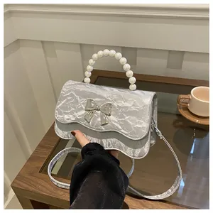 Close-up of silver textured handbag featuring pearl handle and metallic bow detail