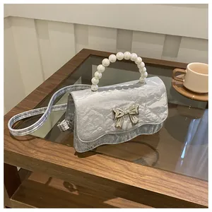 Detail of silver metallic textured handbag with pearl handle and metal bow decoration