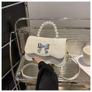 Close-up of white ruffled crossbody bag with pearl handle and silver butterfly buckle