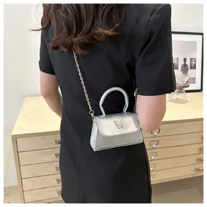 Détail d'un mini sac argenté avec boucle papillon et bandoulière en chaîne dorée