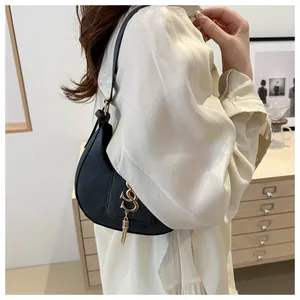 Vue latérale du sac hobo noir en cuir avec logo doré et pompon porté par un mannequin