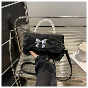 Detail of black crossbody bag with pleated texture, silver bow buckle and pearl handle