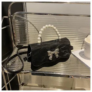 Detail of black pleated crossbody bag with pearl handle and silver metal butterfly knot