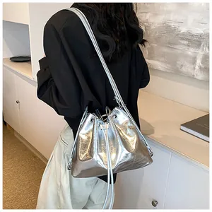 Silver metallic bucket bag with drawstring closure worn by model in minimalist room