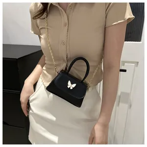 Gros plan d'un mini sac noir avec ornement papillon blanc et bandoulière en chaîne dorée