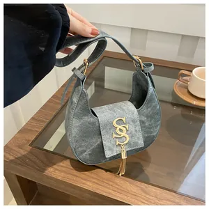 Détail du sac croissant bleu-gris avec texture denim et breloque logo doré chic