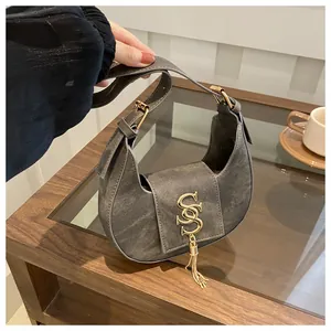 Détail du sac croissant en denim gris avec logo S doré et pendentif à franges stylé