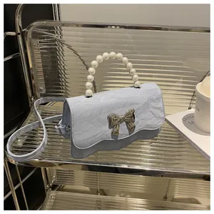 Detail of light blue pearl handle bag with metallic butterfly buckle and wavy flap design