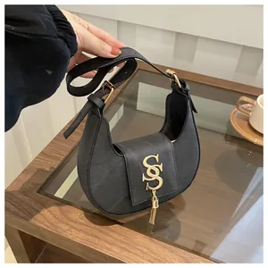 Détail du sac hobo en cuir Saffiano noir avec logo SS doré et pompon sur une table