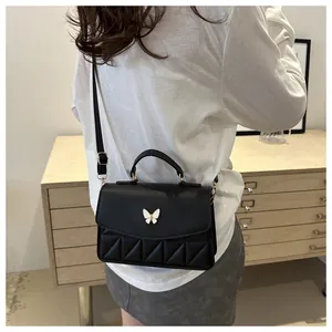 Detail of black crossbody bag with white butterfly metal buckle and quilted pattern