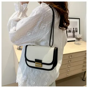 Detail of a beige saddle bag with black leather trim and gold lock shown on model