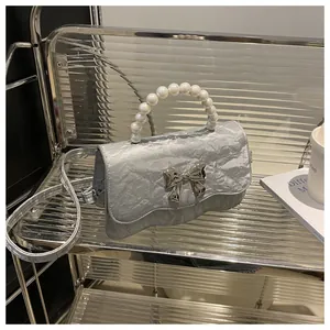 Close-up of silver pleated handbag with pearl handle and metal bow decoration