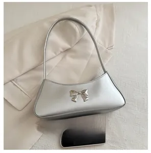 Dettaglio del fiocco d'argento sulla borsa a spalla metallica e blazer beige