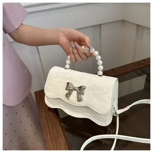 Detail of cream crossbody bag with pearl handle and silver butterfly ornament