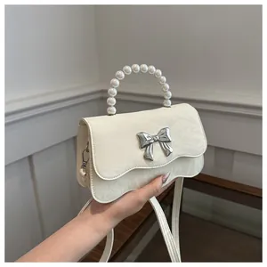 Detail of cream mini bag featuring faux pearl handle and silver butterfly buckle accent
