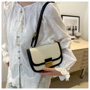 Detail of color-block saddle bag featuring beige canvas, black leather trim, and metal clasp