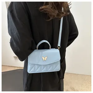 Detail showing light blue quilted crossbody bag with butterfly buckle on black outfit
