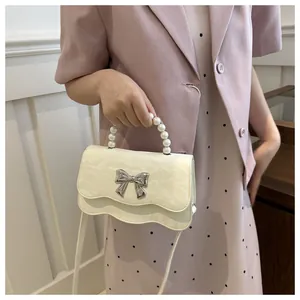 Detail of cream white mini crossbody bag with pearl handle and silver bow decoration