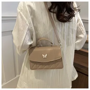 Detailed view of beige crossbody bag featuring metal butterfly clasp and quilted pattern