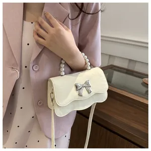 Detail of cream glossy handbag featuring a bow ornament and elegant pearl handle