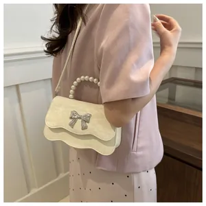 Detail of a creamy white crossbody bag with pearl handle and silver butterfly clasp