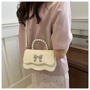 Detail view of cream white handbag with pearl handle and silver butterfly charm decor