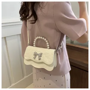 Detail of cream white pleated shoulder bag with pearl handle and silver bow buckle