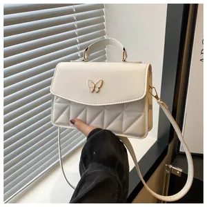 Detail of white PU leather crossbody bag featuring quilted patterns and a butterfly clasp