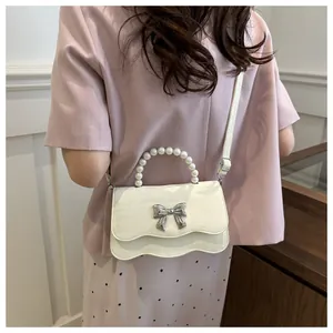 Detail of crossbody bag with pearl handle, metal bow, and wavy flap on a female model