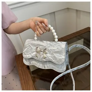 Detail of silver pleated handbag featuring pearl handle and metallic bow decoration