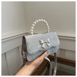 Detail of silver pleated handbag with pearl handle and metal bow decoration
