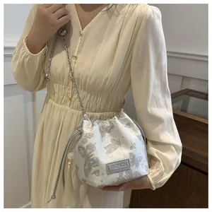 Detail der weißen Beuteltasche mit Schmetterlingsdruck, Perlenquaste und Kettenriemen