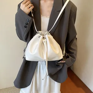 Minimalist white drawstring bucket bag shown on a model in a stylish urban outfit