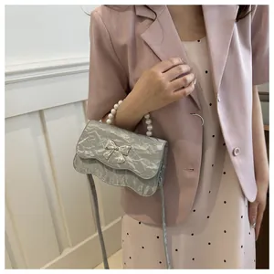Detail of silver metallic pleated crossbody bag with pearl handle and silver bow accent