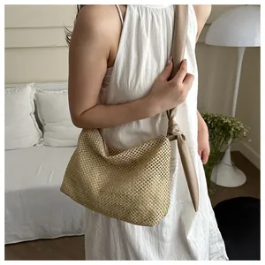 Detail of hollow woven straw tote bag featuring a stylish knotted leather shoulder strap