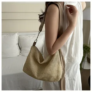 Detail of hollow woven straw tote bag with brown leather strap worn by a model