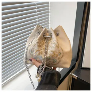 Détail de broderie florale sur sac seau crème avec bandoulière chaîne argentée