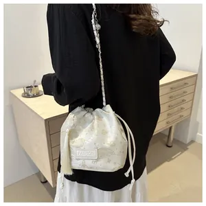 Detail der cremeweißen Beuteltasche mit goldener Schmetterlingsstickerei und Quastenanhänger
