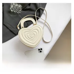 Detail of white heart-shaped crossbody bag with quilted texture and gold metal buckle