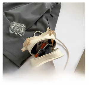 Detail view of cream heart-shaped crossbody bag capacity showing phone and lipstick