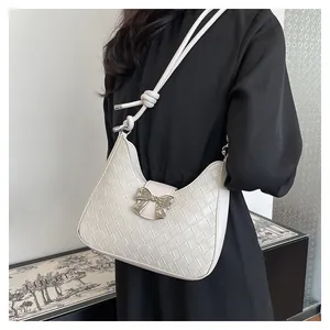 Detail of white woven crescent bag featuring a metallic silver bow and knotted strap