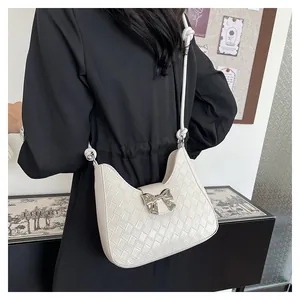 Detail of a creamy white woven crescent shoulder bag with a silver metallic bow and knot strap