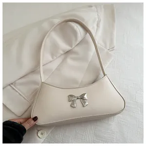 Gros plan d'un sac à bandoulière crème avec nœud argenté et détails métalliques