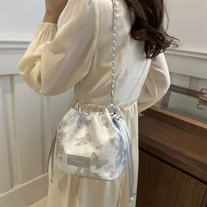 Weiße Eimertasche mit Schmetterlingsdruck und Kettenriemen am Modell im Innenbereich gezeigt