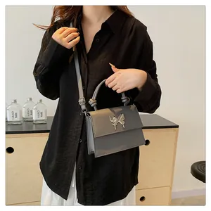 Detalle del bolso gris con broche de mariposa plateado y asa anudada de diseño moderno